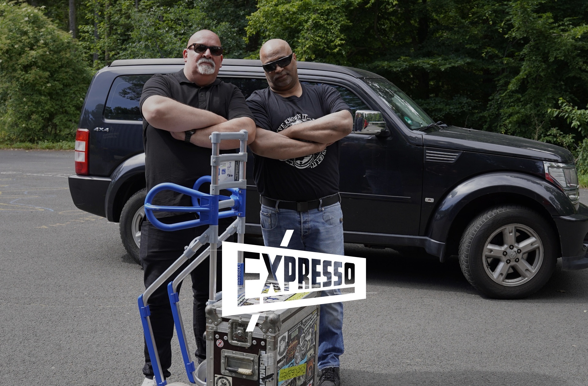 Zwei Männer stehen mit einer beladenen Sackkarre vor einem Auto, im Vordergrund ist das EXPRESSO-Logo zu sehen.