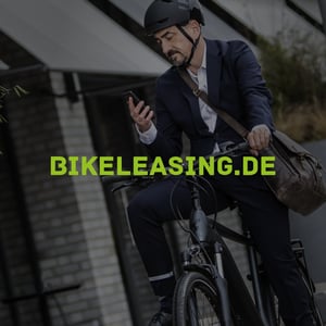 Geschäftsmann im Anzug mit Helm auf Fahrrad blickt auf sein Smartphone.