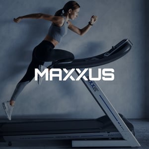 Frau im Sportdress auf Laufband, im Vordergrund ist das MAXXUS-Logo zu sehen.