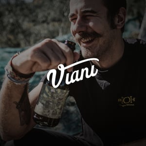 Lächelnder älterer Mann in der Natur mit Weinflasche in der Hand, Viani-Schriftzug im Vordergrund.
